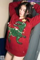 A woman wearing a red sweater with a green dinosaur on it.