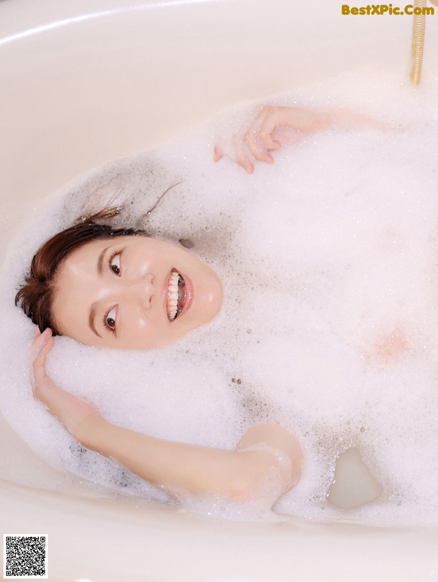 A woman laying in a bathtub with foam on her face.