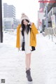 A woman in a yellow jacket is walking in the snow.