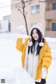 A woman in a yellow jacket and white hat is playing in the snow.