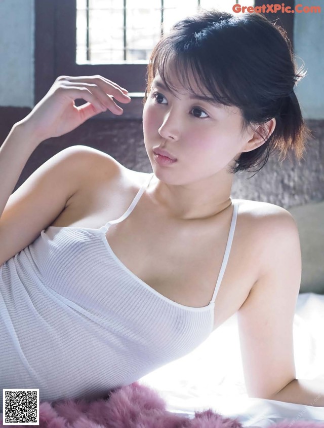 A woman in a white tank top laying on a bed.