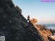 A man standing on top of a rocky cliff next to the ocean.