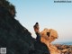 A man taking a picture of a woman on a rock.