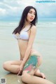 A woman in a white bikini sitting on the beach.