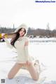 A woman in a white sweater and hat sitting in the snow.