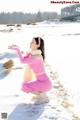 A woman in a pink sweater and skirt crouching in the snow.