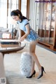 A woman in a blue shirt and denim shorts standing next to a table.