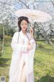 A woman in a pink kimono holding an umbrella in a park.