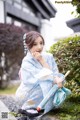 A woman in a blue kimono sitting on the ground holding an umbrella.