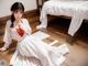 A woman in a white dress sitting on a wooden floor.