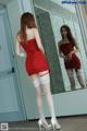 A woman in a red dress and white stockings standing in front of a mirror.