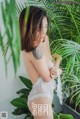 A woman in a white lingerie standing next to a plant.