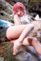 A woman with pink hair sitting on a rock in the water.