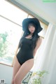 A woman in a black bathing suit and a black hat.