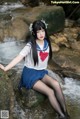 A woman in a school uniform sitting on a rock by a stream.