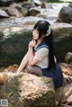 A woman sitting on a rock in the water.