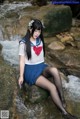 A woman in a school uniform sitting on a rock by a stream.