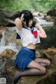 A woman in a school uniform sitting on a rock by a stream.