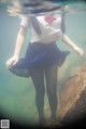 A woman in a white shirt and blue skirt is underwater.