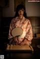 A woman in a kimono sitting at a table with a fan.