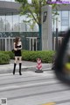 A woman in a black dress and thigh high boots is walking down the street.