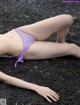 A woman in a purple bikini laying on the ground.