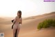 A nude woman standing in the middle of a desert.